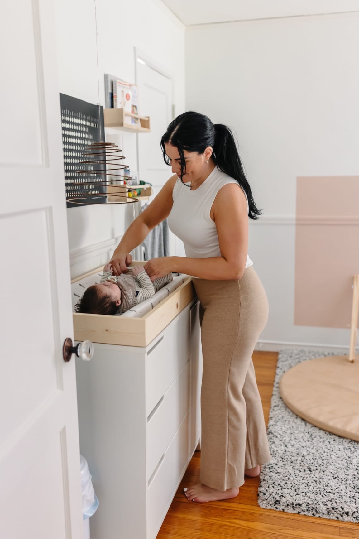 Ashlee barefoot in a calm nursery, attentively tending to a baby on the changing table