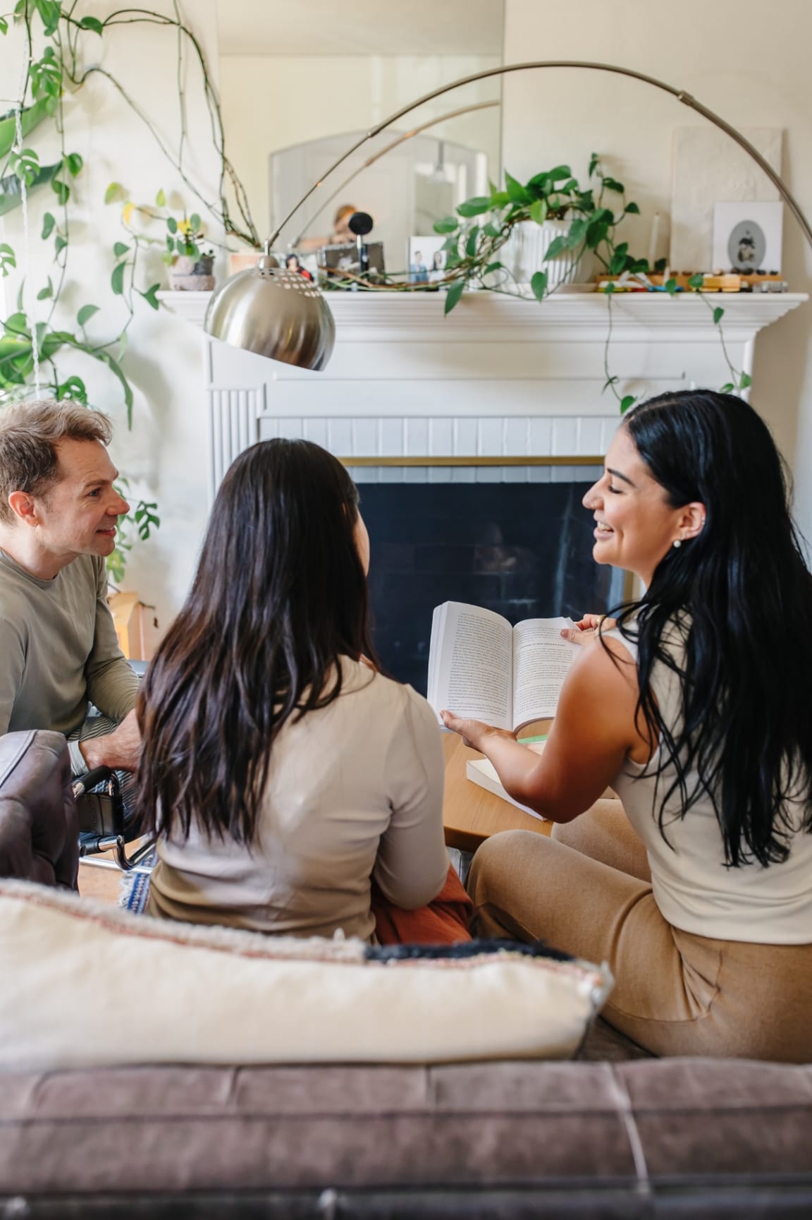 Ashlee reading aloud from a book to two parents during an attentive postpartum education session in a sunlit living room