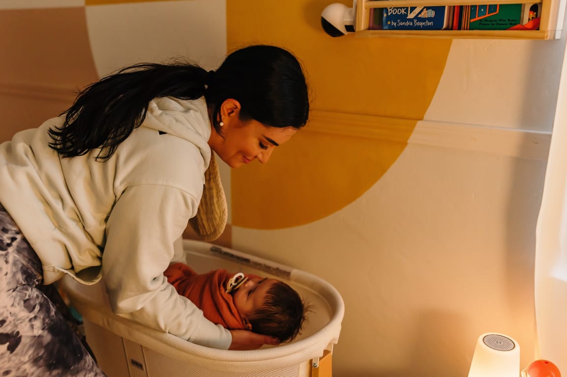 Ashlee leaning over a bassinet, sharing a quiet moment of eye contact with a baby looking up at her