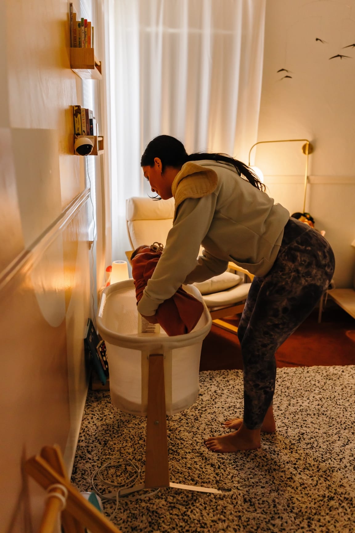 Ashlee gently lowering a swaddled baby into a bassinet in a warmly lit nursery at night