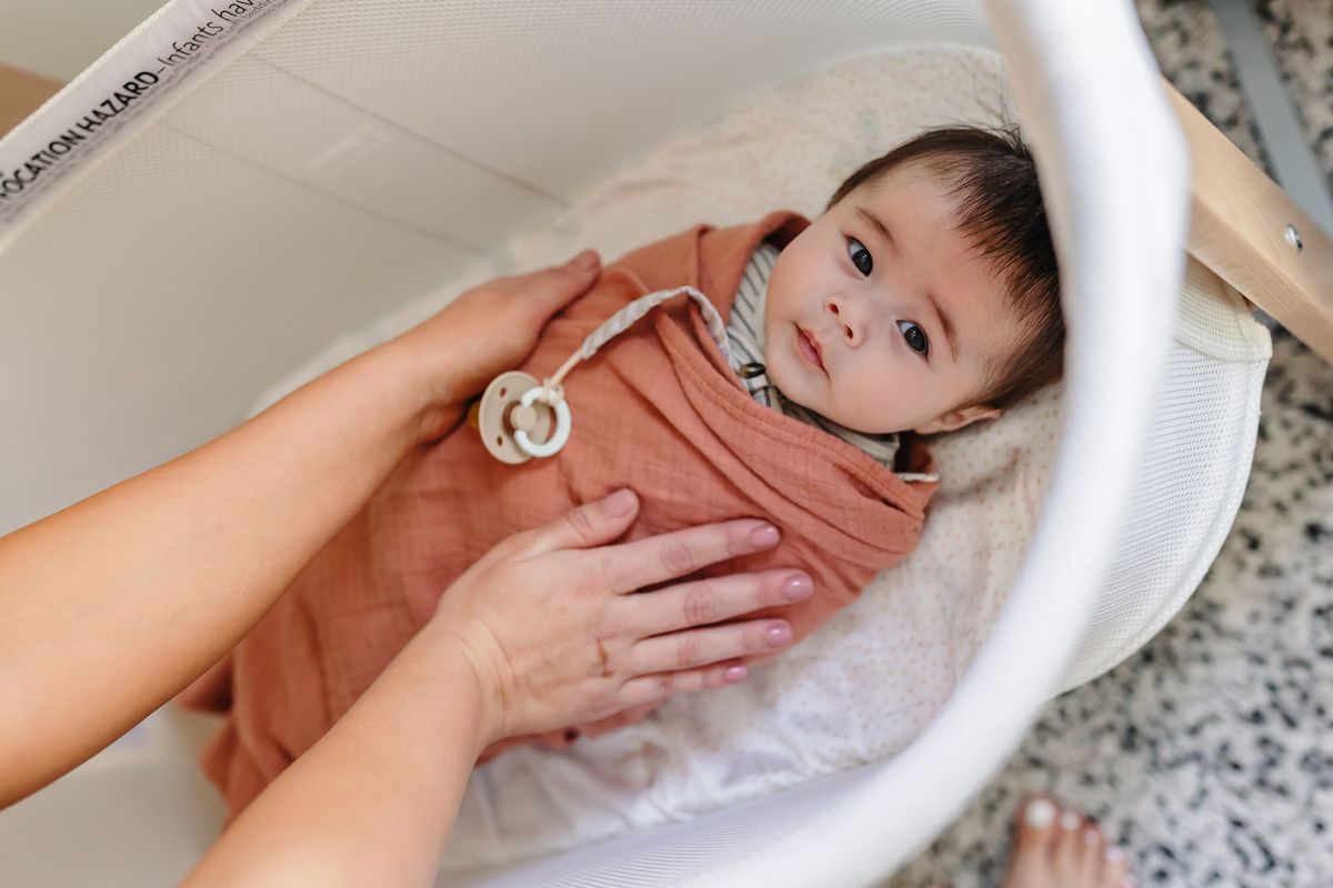 Top-down view of hands settling a swaddled newborn into a bassinet — safe sleep and responsive care