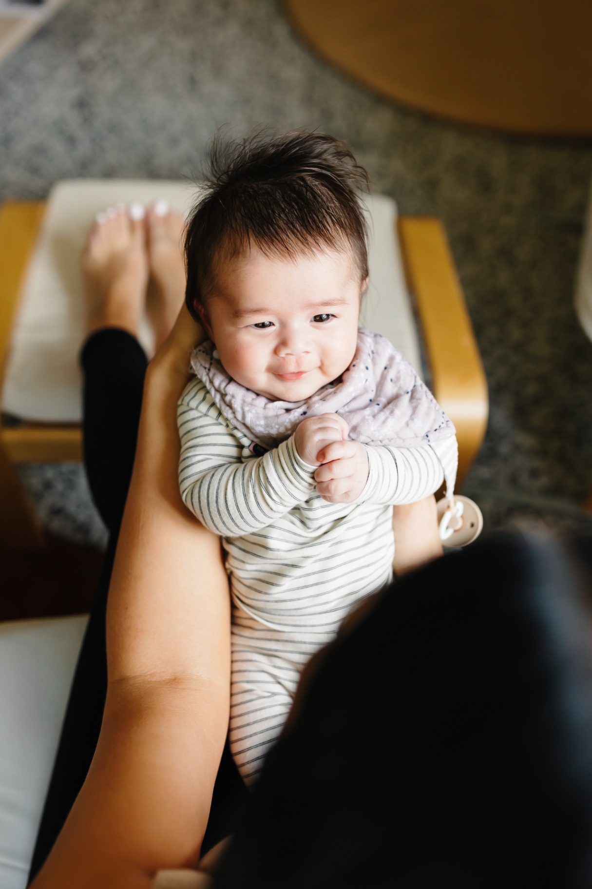 A newborn in a striped onesie smiling up while held gently in a caregiver's hands