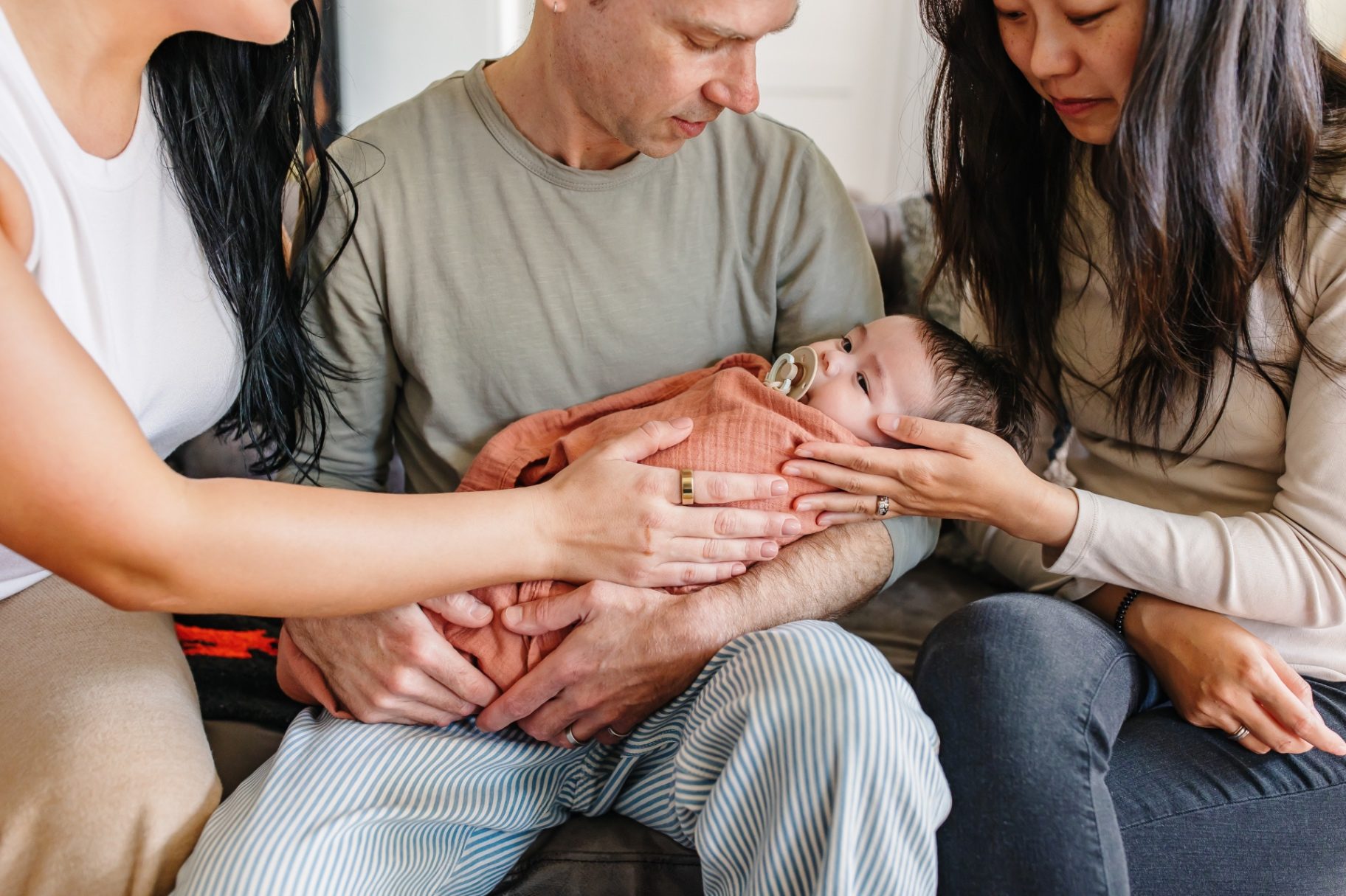 Parents' and Ashlee's hands resting together around a swaddled newborn
